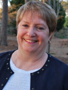 White woman with short hair, wearing a top, sweater, and small hoop earrings, smiling