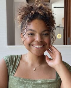 Young woman with brown skin and curly hair in an updo dressed nicely