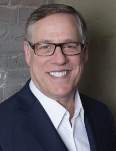 white man with graying temples wearing glasses, a collared shirt, and a suit jacket